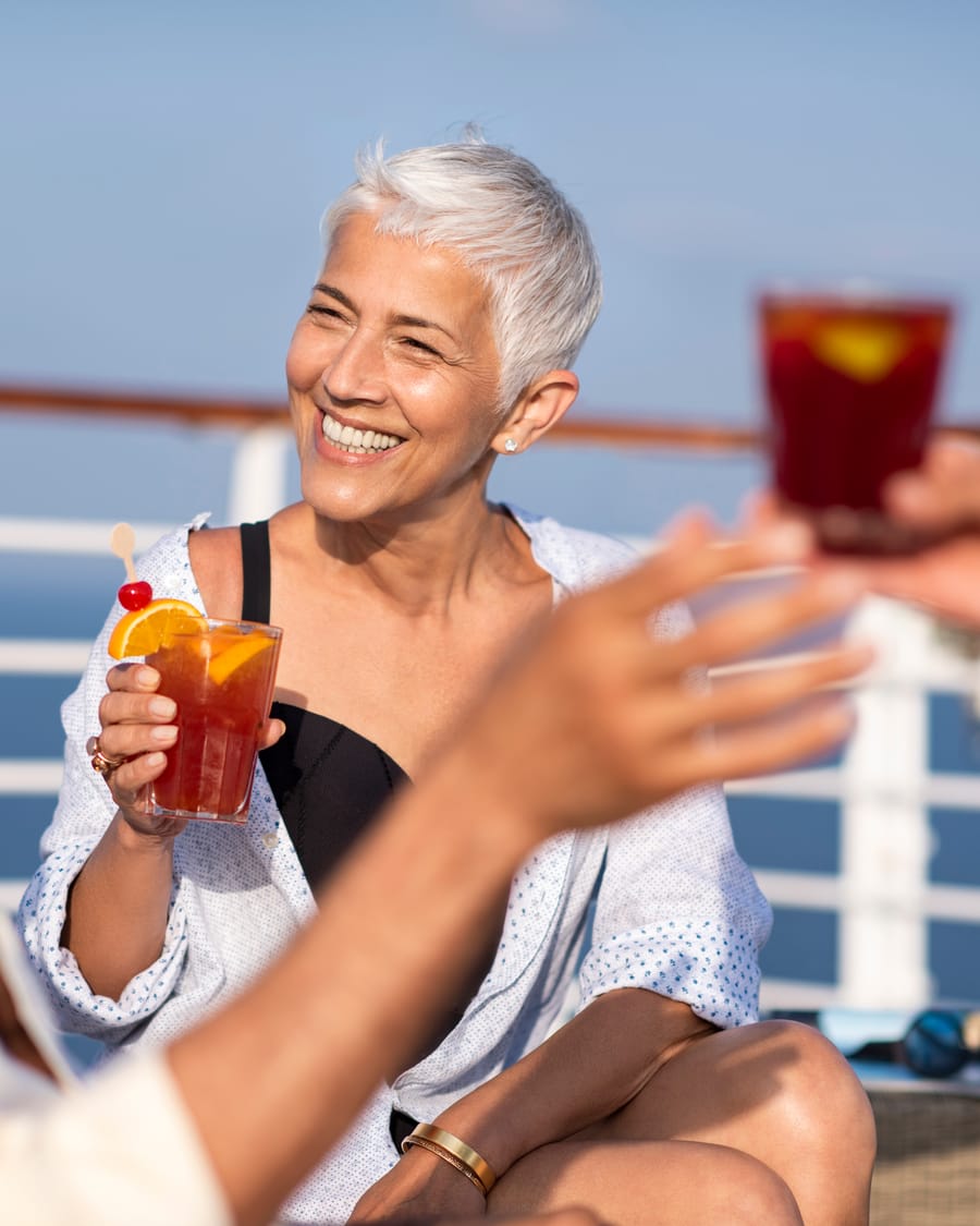 Mulher sorridente com um coquetel no convés, com o mar ao fundo